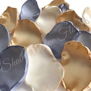 May include: A collection of silk rose petals in ivory, gold, and gray colors. The petals are arranged in a pile, showing the different colors and textures.