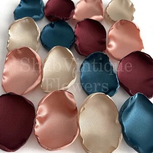 May include: Assortment of silk flower petals in burgundy, teal, blush, and ivory colors. The petals are arranged in a random pattern on a white surface.
