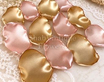 Puede incluir: Una colección de pétalos de flores artificiales en tela de satén color oro metálico y rosa suave. Los pétalos están dispersos, con un brillo suave y reflectante y bordes redondeados. El texto ShabVintique Flowers está superpuesto en el centro.