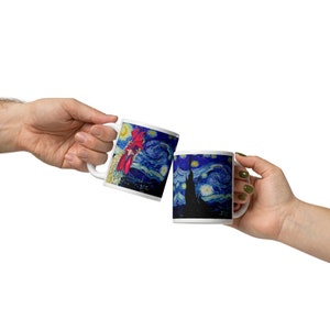 Könnte beinhalten: Zwei weiße Keramikbecher mit Henkeln, jeweils mit einem Design, das von Van Goghs "Sternennacht" inspiriert wurde. Auf einem Becher ist ein roter Hahn abgebildet, auf dem anderen eine schwarze Silhouette einer Kirche. Die Becher werden hochgehalten.