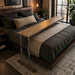 May include: A wooden bed tray with metal legs, resting on a bed with dark gray bedding and a beige throw. The tray is rectangular and has a natural wood finish. The bed is in a room with exposed brick and a large window.