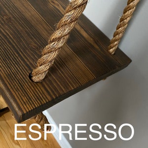Puede incluir: Un estante de madera te&ntilde;ido de marr&oacute;n oscuro suspendido por gruesas cuerdas de fibra natural trenzada. El estante rectangular presenta una veta de madera visible y est&aacute; asegurado por cuerdas que pasan por orificios circulares. La palabra ESPRESSO aparece debajo.