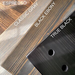 Puede incluir: Cuatro tablas de madera que muestran diferentes acabados de tinte etiquetados como Espresso, Classic Gray, Black Ebony y True Black. La veta de la madera es visible en cada pieza, y la tabla True Black tiene dos orificios circulares perforados.