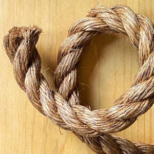 May include: Close-up of a thick, natural fiber rope coiled in a circle. The rope is a light brown color and has a rough texture.