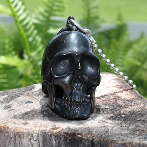 May include: A black skull keychain with a silver chain. The skull is detailed with eye sockets, a nose, and a mouth.
