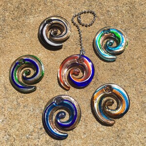 Puede incluir: Seis abalorios de espiral de vidrio de colores con una cadena plateada. Los abalorios son en tonos de azul, verde, dorado y rojo.