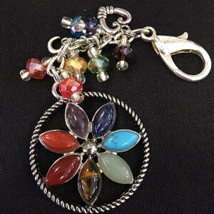 May include: A silver charm bracelet with a flower charm featuring seven different colored gemstones. The bracelet has a silver lobster clasp and a silver heart charm.