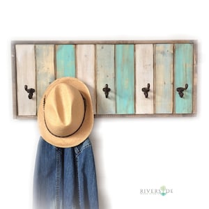 May include: Rustic wooden coat rack with five hooks and a distressed white and blue paint finish. A straw hat and denim jacket are hanging on the hooks.