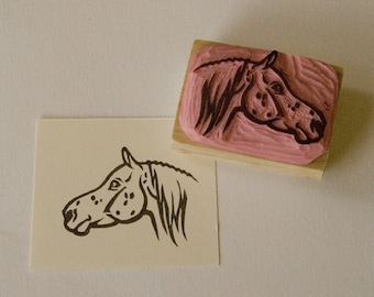 May include: A black and white line drawing of a horse's head with spots on its face. The image is printed on a white card. A wooden block with a pink rubber stamp of the same horse's head is also shown.