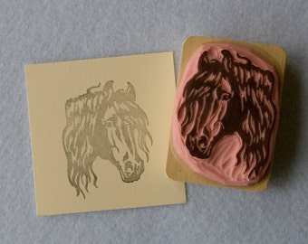May include: A horse head rubber stamp with a wooden handle next to a stamped image of the same horse head. The stamp is pink and brown, and the stamped image is in a light brown color.