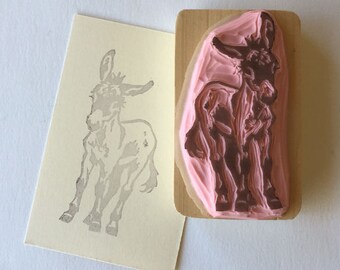 May include: A wooden mounted rubber stamp with a pink background and a brown donkey design. The donkey is standing with its head turned to the side.