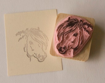 May include: A wooden block with a pink rubber stamp of a horse's head. The horse has a brown mane and a pink nose.