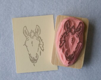 May include: A wooden block with a pink rubber stamp of a donkey's head. The stamp is uninked and shows the design of the donkey's head.