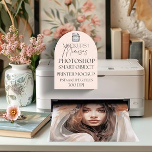 Puede incluir: Una impresora blanca con una impresión de la cara de una mujer que emerge de la bandeja de papel. La impresora está sobre una superficie blanca con un jarrón de flores rosas y un libro. Una pegatina rosa en la impresora dice "Mockups and Mimosa, Photoshop Smart Object Printer Mockup, PSD and JPEG Files, 300 DPI".