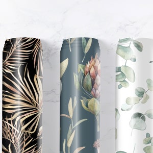 May include: Three rolls of fabric with different floral patterns. The first roll features a black background with gold palm leaves. The second roll has a dark blue background with a floral pattern of pink and green flowers. The third roll has a white background with a green eucalyptus leaf pattern.