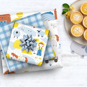 May include: A stack of three gift wrap papers with a farm theme. The top paper features a blue and white plaid pattern, the middle paper has a white background with yellow hay bales, a blue and white plaid border, and illustrations of farm animals, and the bottom paper has a white background with a red barn, a blue and white plaid border, and illustrations of farm animals. The papers are tied together with a silver bow.