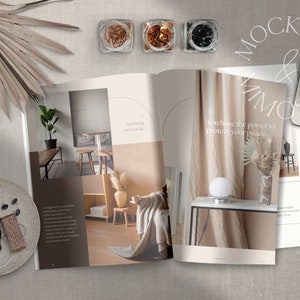May include: Open magazine with interior design photos and text that reads "Just living my best life" and "You have the power to protect your peace."  The magazine is on a beige linen surface with a palm leaf, a plate with a pair of earbuds and two spools of twine, and a white smartphone.