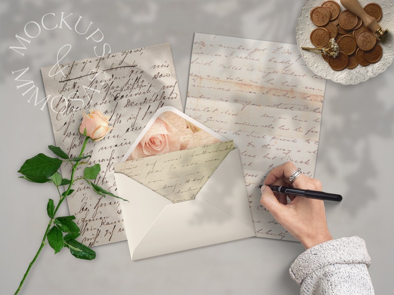 May include: A white envelope with a pink rose design on the front. The envelope is open and there is a handwritten letter inside. The letter is on a table with a pen and a hand writing on it.