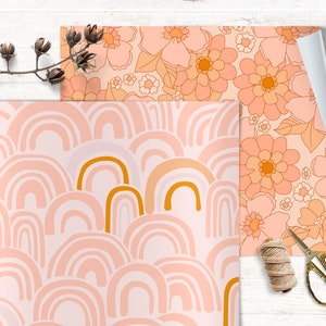 May include: Two sheets of wrapping paper with different patterns. One sheet features a pink and orange floral design. The other sheet features a pink and gold rainbow pattern.