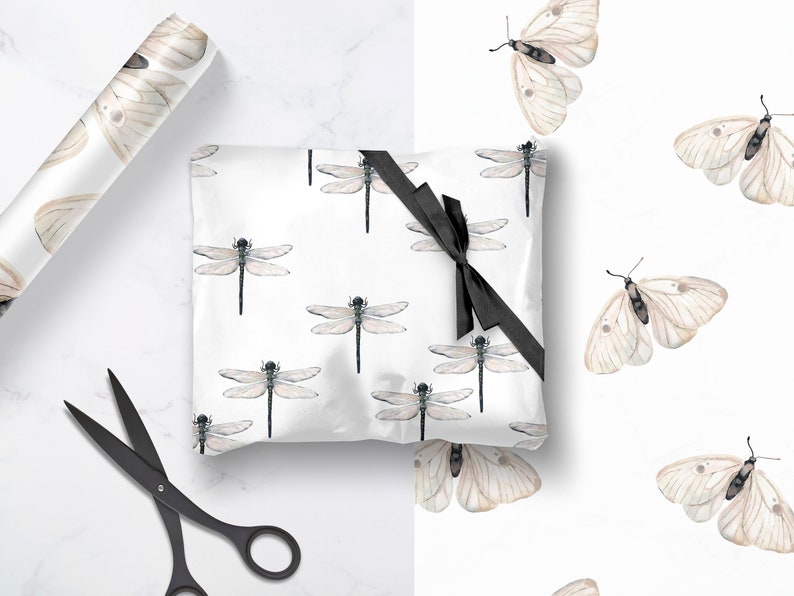 May include: White wrapping paper with a repeating pattern of delicate brown dragonflies and butterflies. A black ribbon is tied around the paper, and a pair of black scissors are lying on a white surface.