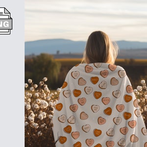 May include: A white blanket with a pattern of pink and orange candy hearts. The hearts have various messages on them, including "Love You", "Hug Me", "Sweet", "XOXO", "Cute Pie", "Text Me", and "Kiss Me".