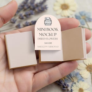 May include: A miniature book mockup with a beige cover and pages, displayed open and closed. The image includes text that reads "MINI BOOK MOCKUP DRIED FLOWERS 300 DPI MOCKUPS + MIMOSAS". Dried flowers are in the background.