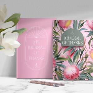 May include: Two pink journals with the text "My Journal of Thanks" on the front. One journal has a simple design with a circle and lines. The other journal has a floral pattern with pink flowers and green leaves.