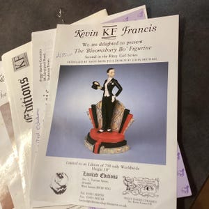 May include: A ceramic figurine of a person in formal wear, holding a hat, on a decorative base. The figurine is part of the 'Ritzy Girl Series' and is 25.4 cm tall. The image includes promotional materials from 'Peggy Davies Ceramics'.
