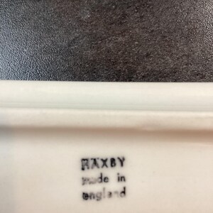 May include: A white ceramic surface featuring a black stamped mark that reads HAXBY made in england. The text is arranged in three lines with the brand name at the top, followed by the production origin in lowercase letters below it.