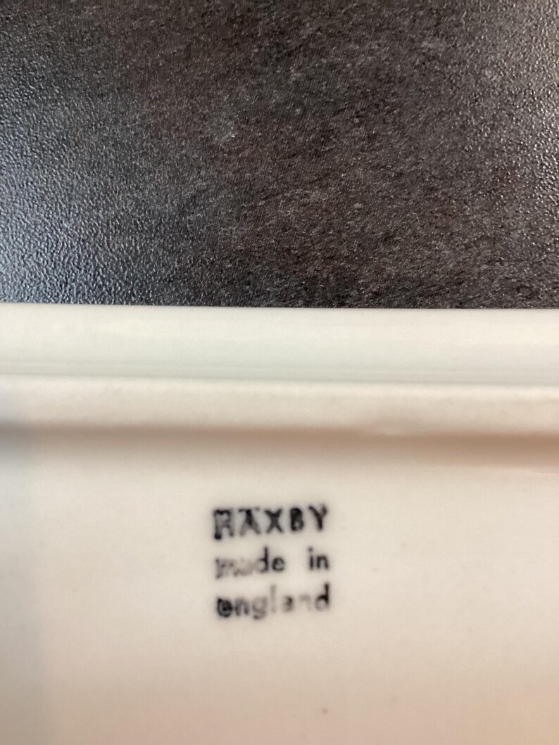 May include: A white ceramic surface featuring a black stamped mark that reads HAXBY made in england. The text is arranged in three lines with the brand name at the top, followed by the production origin in lowercase letters below it.