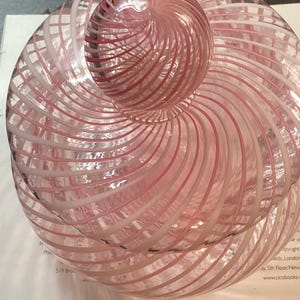 May include: A clear glass jar with a lid, featuring a swirling pattern of opaque white and translucent pink stripes. The jar has a rounded body and a matching spherical knob on top, with the glass design creating a continuous spiral effect.
