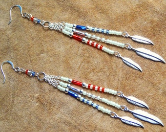 May include: Dangling earrings with a Native American theme. Each earring features a silver-tone hook, chain, and three beaded strands in red, white, and blue. Silver feather charms dangle from the ends of the strands.