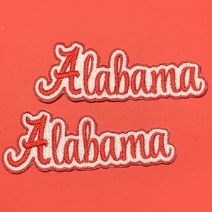 May include: Two embroidered fabric patches featuring the word Alabama in a red cursive script font with a white border. The lettering is stitched with red thread on a white background, creating a distinct outline for each letter in this set.