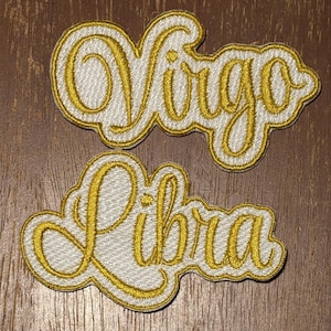 May include: Two embroidered patches featuring the words Virgo and Libra in a cursive script. The lettering is rendered in a metallic gold thread with a white background and a gold border, creating a distinct outline for each zodiac sign name.