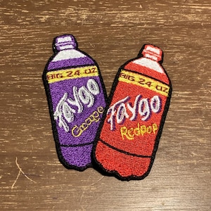 May include: Two embroidered patches in the shape of soda bottles. One is purple with "Faygo Grape" text, the other is red with "Faygo Redpop" text. Both patches have "BIG 24 OZ" text.