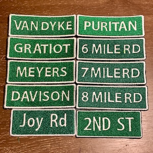 May include: A collection of ten rectangular embroidered patches featuring green backgrounds with white borders and white text. The patches display street names including Van Dyke, Puritan, Gratiot, 6 Mile Rd, Meyers, 7 Milerd, Davison, 8 Mile Rd, Joy Rd, and 2nd St.