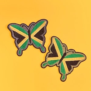 Peut inclure: Deux écussons en forme de papillon avec le drapeau jamaïcain. Les écussons sont verts, noirs et jaunes, avec un contour gris. Le fond est jaune uni.