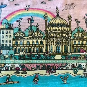 Pu&ograve; includere: Un'illustrazione colorata di una citt&agrave; costiera con un grande edificio al centro. L'edificio ha un tetto a cupola ed &egrave; circondato da edifici pi&ugrave; piccoli. C'&egrave; un arcobaleno nel cielo e le persone si godono la spiaggia.