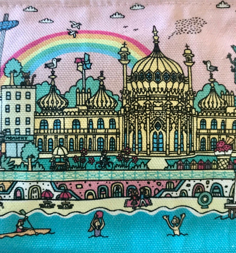 Pu&ograve; includere: Un'illustrazione colorata di una citt&agrave; costiera con un grande edificio al centro. L'edificio ha un tetto a cupola ed &egrave; circondato da edifici pi&ugrave; piccoli. C'&egrave; un arcobaleno nel cielo e le persone si godono la spiaggia.