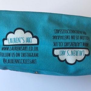Pu&ograve; includere: Una pochette in tela blu chiaro con un design a nuvola bianca e il testo "LAUREN'S ART" in nero. La pochette ha l'indirizzo del sito web "www.LAURENSART.CO.UK" e l'account Instagram "@LAURENNICKLESSART" stampati su di essa.
