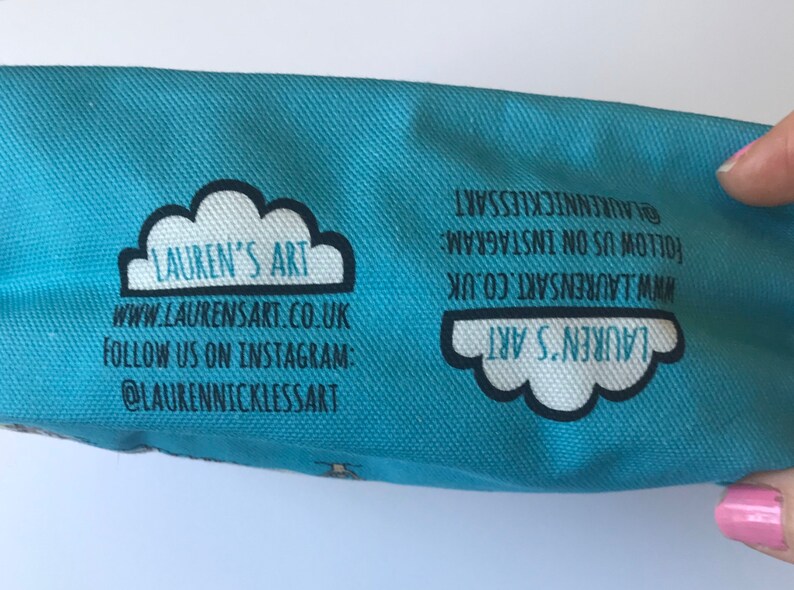 Pu&ograve; includere: Una pochette in tela blu chiaro con un design a nuvola bianca e il testo "LAUREN'S ART" in nero. La pochette ha l'indirizzo del sito web "www.LAURENSART.CO.UK" e l'account Instagram "@LAURENNICKLESSART" stampati su di essa.