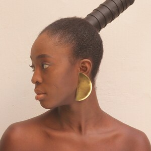May include: A person with short black hair wearing large gold half-circle earrings.