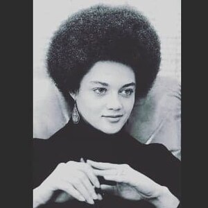 May include: Black and white portrait of a woman with a large afro hairstyle. She is wearing a black turtleneck sweater and has a serious expression on her face.