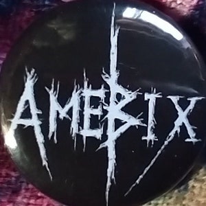 May include: A black and white button with the word "AMERIX" in a stylized font.