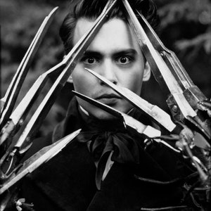 May include: A black and white photo of a person with sharp, metal blades in front of their face. The blades are arranged in a triangular shape, and the person's eyes are visible through the blades.