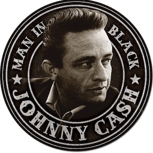 May include: Black and white circular metal sign with the text "Johnny Cash Man in Black" in a circle around a portrait of Johnny Cash.