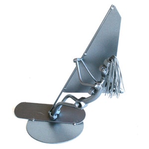 May include: A silver metal sculpture of a person windsurfing. The sculpture is made of nuts, bolts, and other metal pieces. The person is holding a sail and is standing on a board.