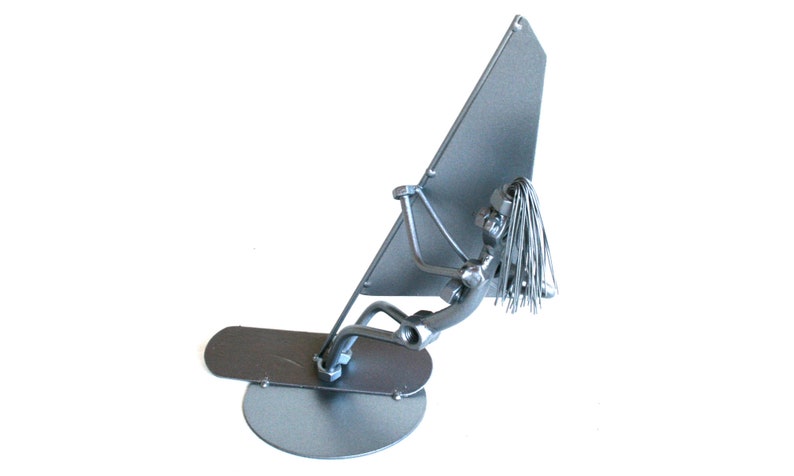 May include: A silver metal sculpture of a person windsurfing. The sculpture is made of nuts, bolts, and other metal pieces. The person is holding a sail and is standing on a board.