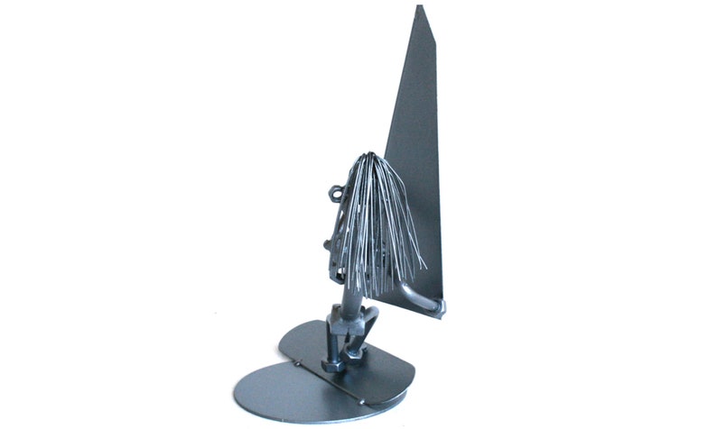 May include: A silver metal sculpture of a person windsurfing. The sculpture is made of thin metal strips and has a simple, abstract design.