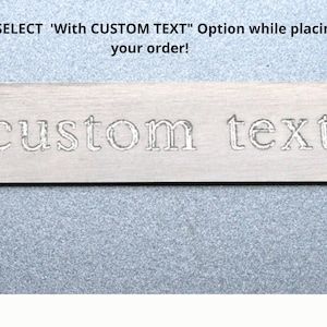 May include: Close-up of a silver metal tag with the words "custom text" engraved on it.